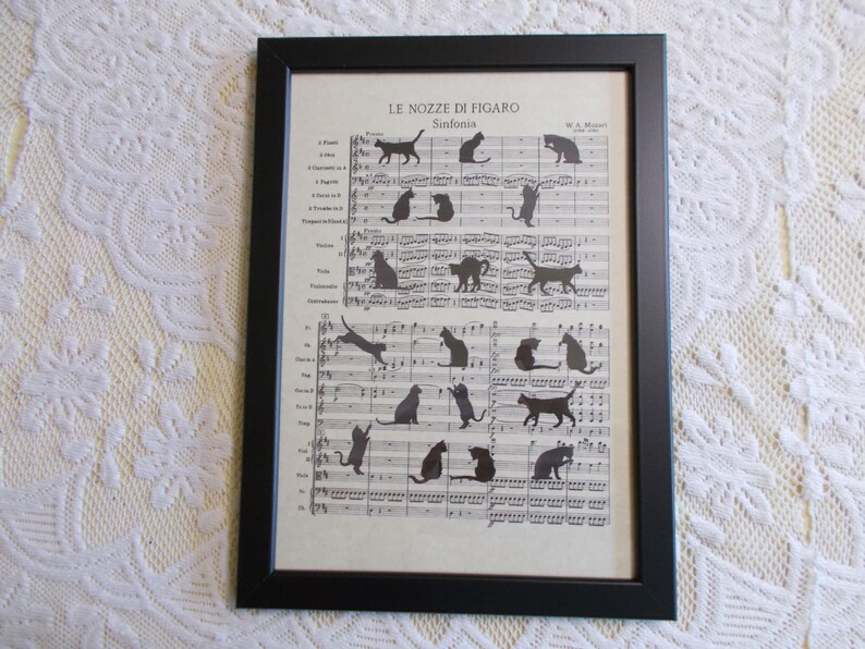 May include: A framed print of sheet music with the title "Le Nozze di Figaro" by W.A. Mozart. The music is decorated with black cat silhouettes in various poses.