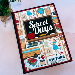 May include: A scrapbook album with a school theme. The cover features a black chalkboard with the words "School Days" and a red apple. The background is decorated with school-related images, including a school bus, pencils, and a globe.