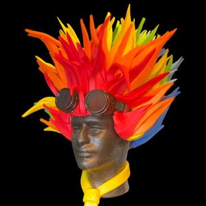 May include: A colourful, spiky wig made of foam, with red, orange, yellow and blue sections. The wig is worn on a mannequin head with a yellow necktie and goggles.
