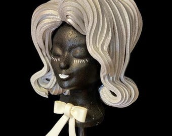 May include: A silver wig with a bouffant style, worn on a black mannequin head with a white bow.