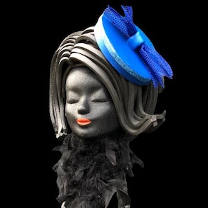 May include: A black foam mannequin head with a blue and black hat. The hat is a round, flat, blue disc with a black bow on top. The mannequin has a black feather boa around the neck.