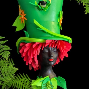 Puede incluir: Un sombrero de espuma verde con flores y hojas, una peluca de espuma roja y una cara de espuma negra. El sombrero tiene una abertura de casita de pájaros con un pájaro pequeño dentro.