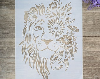 May include: A white stencil of a lion's face with floral designs around it. The lion's face is detailed with a mane, nose, and eyes. The floral designs are intricate and include leaves, flowers, and vines.