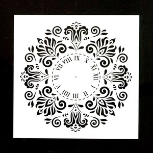 May include: Black and white stencil of a clock face with Roman numerals surrounded by a decorative floral design.