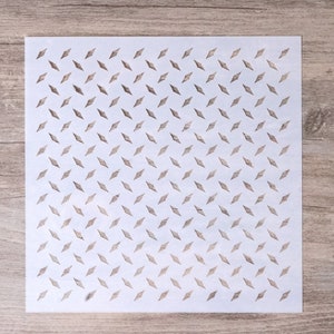 May include: White stencil with a repeating pattern of small diamond shapes cut out. The stencil is on a light brown wooden surface.
