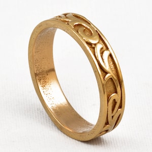 Peut inclure: Une bague dorée avec un motif tourbillonnant complexe gravé autour de l'anneau. La bague a une finition lisse et polie et un design classique. La bague est un bijou.