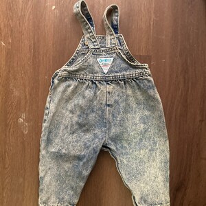 Pode incluir: Macac&atilde;o de ganga azul claro lavado com &aacute;cido com al&ccedil;as ajust&aacute;veis e um patch com o logotipo OshKosh B'Gosh.