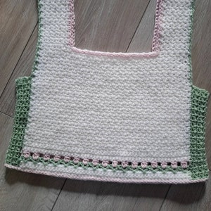 May include: A white crochet top with a green and pink trim. The top has a square neckline and a cropped length.