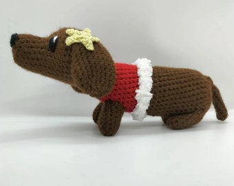 May include: A brown crocheted dachshund wearing a red and white crocheted sweater with a yellow star on its head.