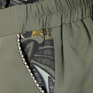 May include: Green pants with a black and white patterned pocket. The pocket has a white trim.
