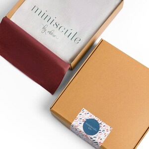 May include: Two cardboard boxes with the logo "miniscule by obrar" printed on them. The top box is open and has a red tissue paper lining. The bottom box is closed and has a colorful sticker with the same logo on it.