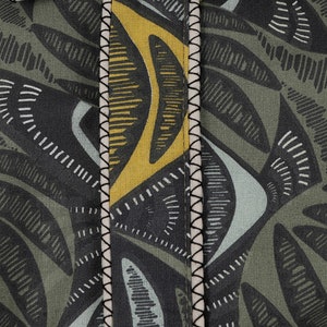 May include: Close-up of a green, yellow, and blue patterned fabric with a black stitched seam. The fabric has a geometric design with abstract shapes.