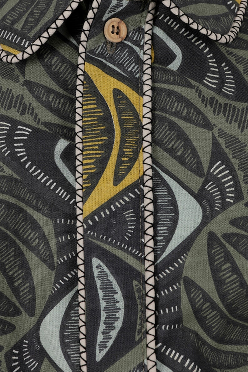 May include: Close-up of a green, yellow, and blue patterned fabric with a black stitched seam. The fabric has a geometric design with abstract shapes.