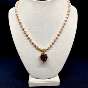 以下が含まれることがあります： 金色のワイヤーで包まれた濃い赤色の宝石がついた、繊細な真珠のネックレスです。
