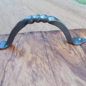 May include: A twisted metal handle with pointed ends, attached to a wooden surface.