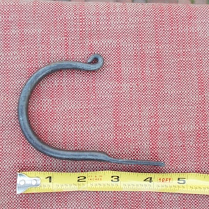 May include: A black metal hook with a curved shape and a pointed end. The hook is measured with a tape measure, showing it is approximately 4 inches long.