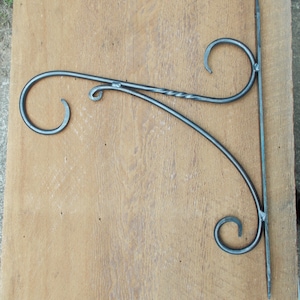 May include: A black metal wall-mounted shelf bracket with two decorative scrolls. The bracket is designed to hold a shelf or other object.