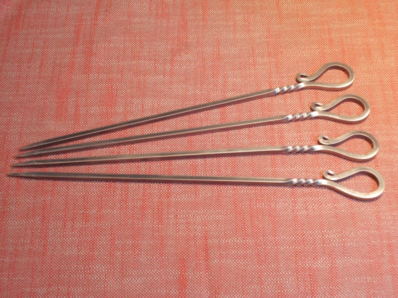 Puede incluir: Cuatro pinchos de metal plateado con mangos retorcidos. Los mangos tienen forma de bucle con un rizo decorativo.