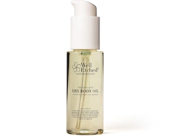 May include: A clear glass bottle of Well Etched Dry Body Oil with a white pump dispenser. The label features the brand name and product details, including "Weightless Dry Body Oil" and the size, 2 oz / 59 ml. The oil is a light amber color.