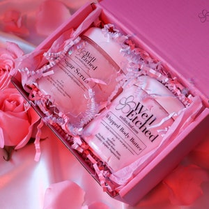 May include: Pink gift box with white tissue paper and two jars of body care products. The jars are labeled "Well Etched" and contain "Sugar Scrub" and "Whipped Body Butter".