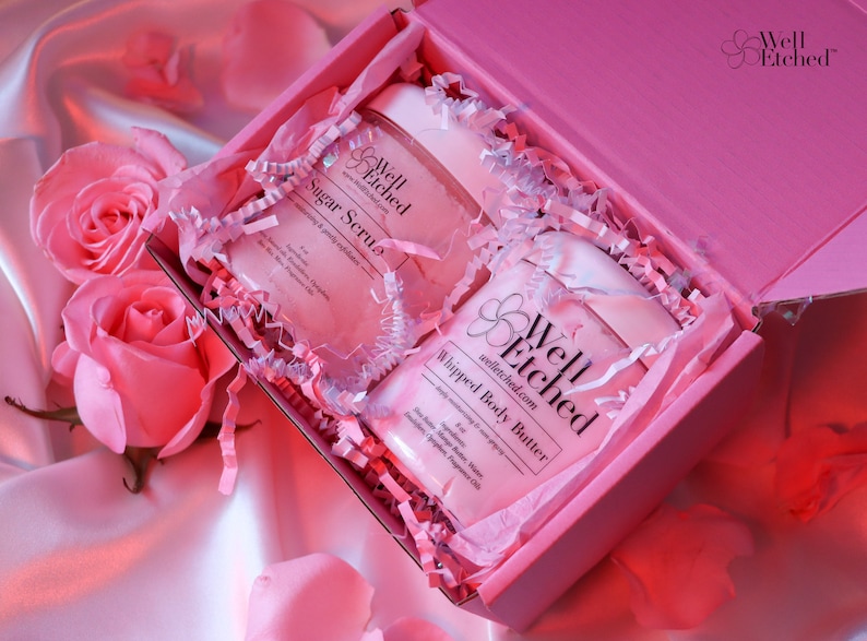 May include: Pink gift box with white tissue paper and two jars of body care products. The jars are labeled "Well Etched" and contain "Sugar Scrub" and "Whipped Body Butter".