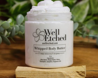 May include: A white jar of "Whipped Body Butter" with a swirl of white cream on top. The jar has a label with the text "Well Etched" and "welletched.com". The jar is 8 oz. and sits on a wooden stick.
