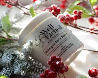 May include: A white jar of whipped body butter with the text "Well Etched" and "Whipped Body Butter" on the label. The jar is surrounded by a snowy green branch with red berries.