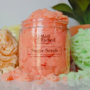 May include: A glass jar filled with pink sugar scrub. The label reads "Well Etched" and "Sugar Scrub - moisturizing & gently exfoliates". The ingredients are listed as "Sugar, Natural oils, Emulsifiers, Optiphen, Bees Wax, Mica, Fragrance Oils".