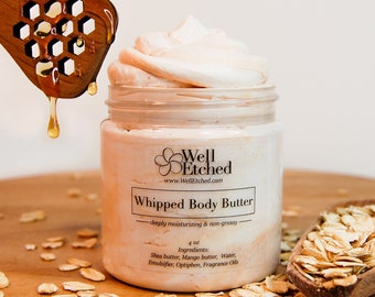 May include: A glass jar of whipped body butter with a white label that reads "Well Etched" and "Whipped Body Butter - deeply moisturizing & non-greasy - 4 oz. Ingredients: Shea butter, Mango butter, Water, Emulsifier, Optiphen, Fragrance Oils". The jar is sitting on a wooden surface with oats scattered around it. A wooden honey dipper with honey dripping from it is in the background.