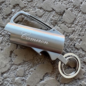 May include: A silver keychain multi-tool with a carabiner clip, bottle opener, and key ring. The name "Cameron" is engraved on the side. The tool is made of brushed metal and is designed for everyday use.