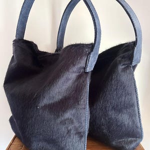 Damentasche aus gestricktem Stoff mit dunkelblauem Fell, kombiniert mit einem Griff und marineblauen Lederdetails.