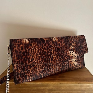 May include: A brown and black leopard print clutch purse with a gold chain strap.