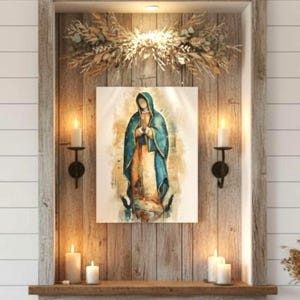 Op de afbeelding: Een religieus kunstwerk in een houten lijst, met een figuur in een blauwe jurk, geplaatst in een houten nis met kaarsen en gedroogde bloemdecoraties. Het kunstwerk is verlicht, wat een vredige sfeer creëert.