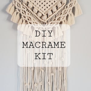 May include: A cream-colored macrame wall hanging with a geometric design and fringe. The text "DIY MACRAME KIT" is overlaid on the piece. The macrame is suspended from a wooden dowel.