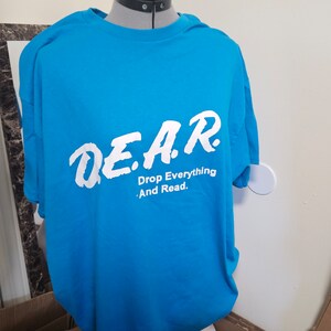 May include: A bright blue t-shirt with white text that reads "D.E.A.R. Drop Everything And Read."