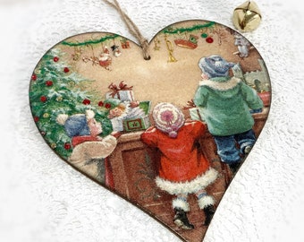 May include: Heart-shaped wooden Christmas ornament featuring a vintage illustration of children looking at gifts. The ornament has a string for hanging and a small gold bell. The illustration includes a Christmas tree and Santa Claus.