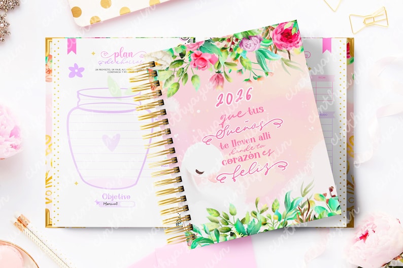 May include: A spiral-bound planner with a floral design and the year 2026 on the cover. The cover features a watercolor illustration with text in Spanish. The open planner shows lined pages and a jar illustration.