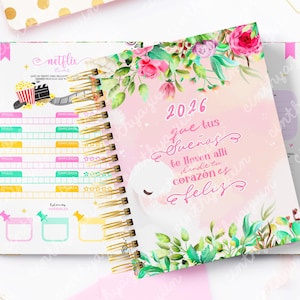 May include: Open spiral-bound planner with a floral cover featuring the year 2026 and a swan illustration. The planner's interior includes sections for Netflix tracking and goal setting, with a gold spiral binding and a pink and gold color scheme.