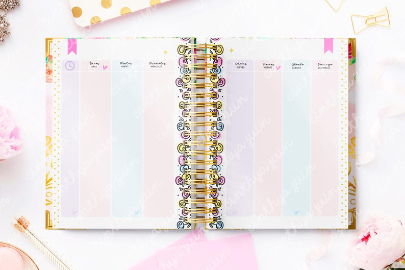May include: Open planner with a gold spiral binding, featuring pastel-colored columns for each day of the week. The pages are decorated with floral and geometric patterns, and the text is in Spanish.