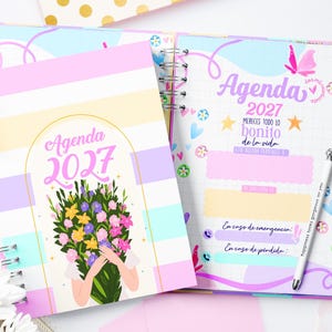 Puede incluir: Una agenda 2027 de espiral con portada de rayas pastel y una ilustración de un ramo de flores. La página interior abierta muestra el texto Agenda 2027, Mereces todo lo bonito de la vida, e incluye secciones para contactos de emergencia y pérdida.