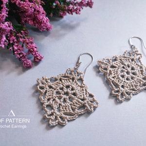 May include: A pair of crocheted earrings with a square shape and a delicate, intricate design. The earrings are beige in color and have silver hooks.