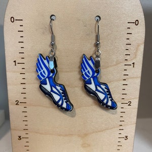 May include: A pair of silver earrings with blue and white running shoe charms. The charms are about 2 inches long and feature a white shoe with a blue wing on the side.