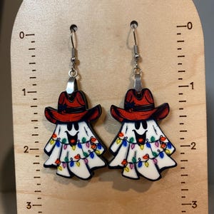 K&ouml;nnte beinhalten: Ein Paar Geisterohrringe mit roten Cowboyh&uuml;ten und bunten Lichtern. Die Ohrringe sind aus Holz und haben silberne Haken.