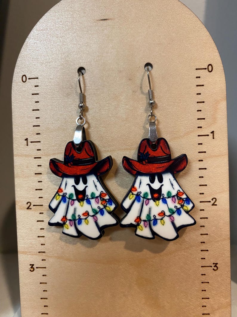 K&ouml;nnte beinhalten: Ein Paar Geisterohrringe mit roten Cowboyh&uuml;ten und bunten Lichtern. Die Ohrringe sind aus Holz und haben silberne Haken.