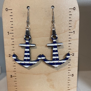 May include: A pair of blue and white striped anchor earrings with gold polka dots. The earrings are hanging from silver hooks.