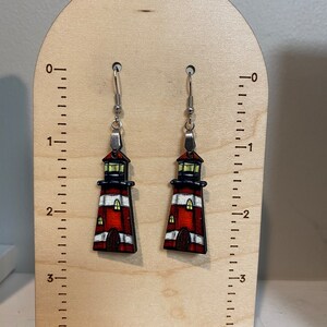 May include: Pair of wooden lighthouse earrings with red, white, and black stripes. The earrings are about 2 inches long and have silver hooks.