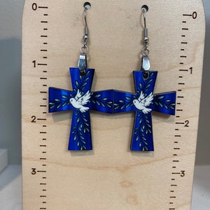 May include: A pair of blue cross earrings with white doves and green leaves. The earrings are approximately 2 inches long.