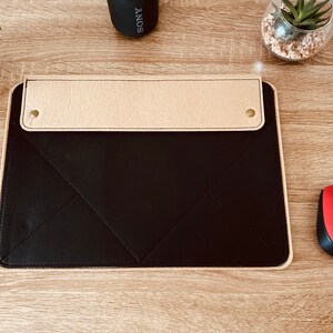 May include: A black leather desk mat with a beige leather flap and two brass accents. The mat has a stitched diamond pattern.