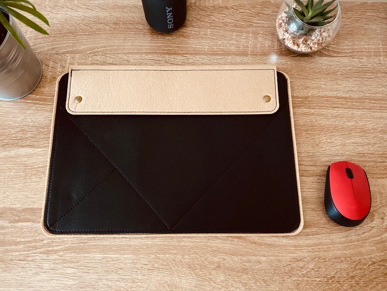 May include: A black leather desk mat with a beige leather flap and two brass accents. The mat has a stitched diamond pattern.