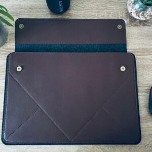 May include: A brown leather laptop sleeve with a flap closure and a soft grey felt lining. The sleeve has gold-coloured metal snaps and a stitched diamond pattern.